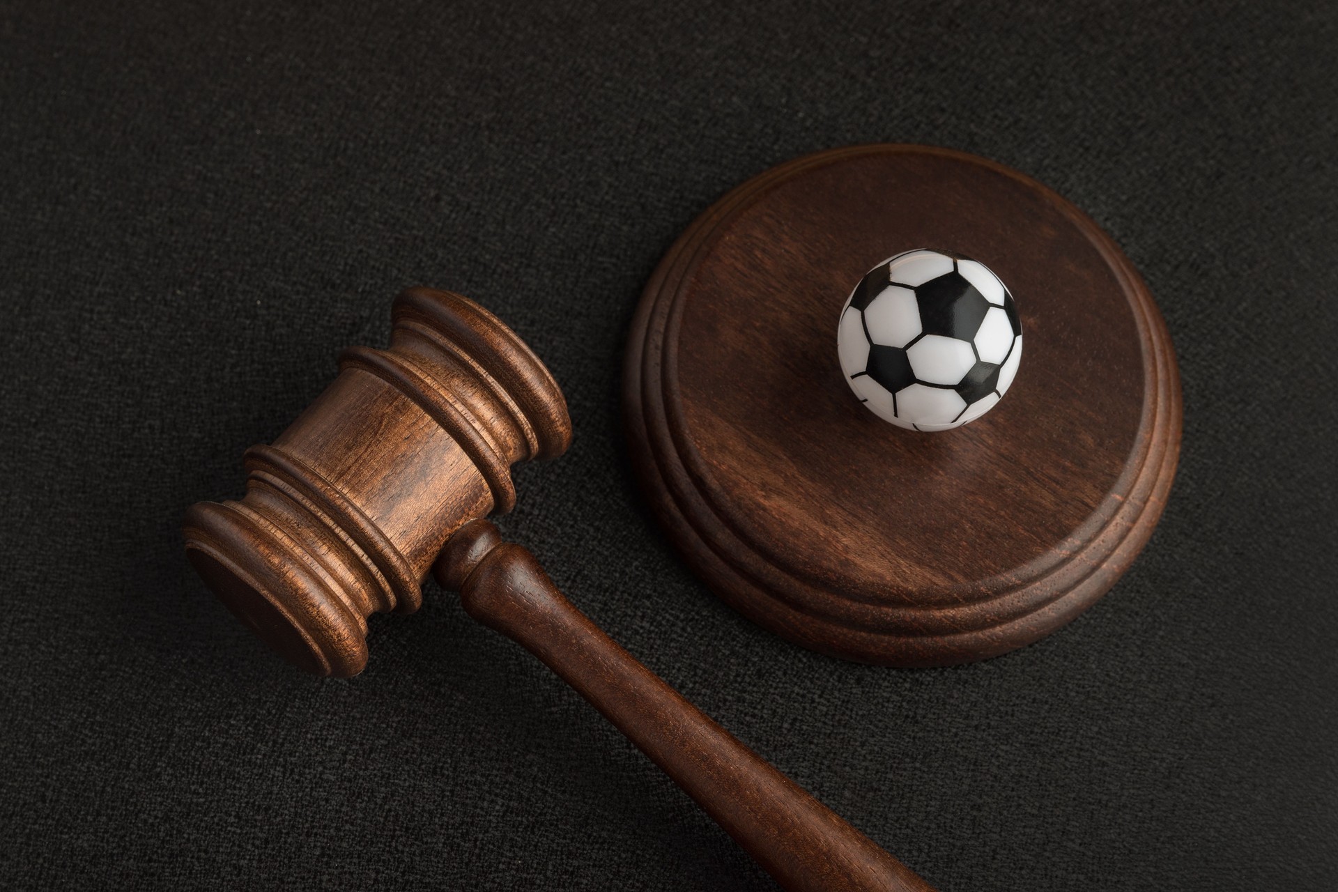 Wooden judge gavel and toy soccer ball. Football coach accused. Concussion lawsuit.